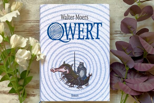 Buch Qwert von Walter Moers auf Holzboden mit Blumen.